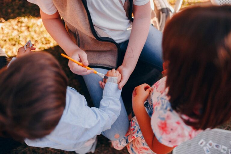 A group of children enjoying applying temporary tattoos together outdoors.