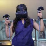A woman using VR headset and controllers for an immersive gaming experience indoors.