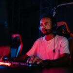 A young man focuses intensely while playing in an online gaming tournament, wearing a headset.